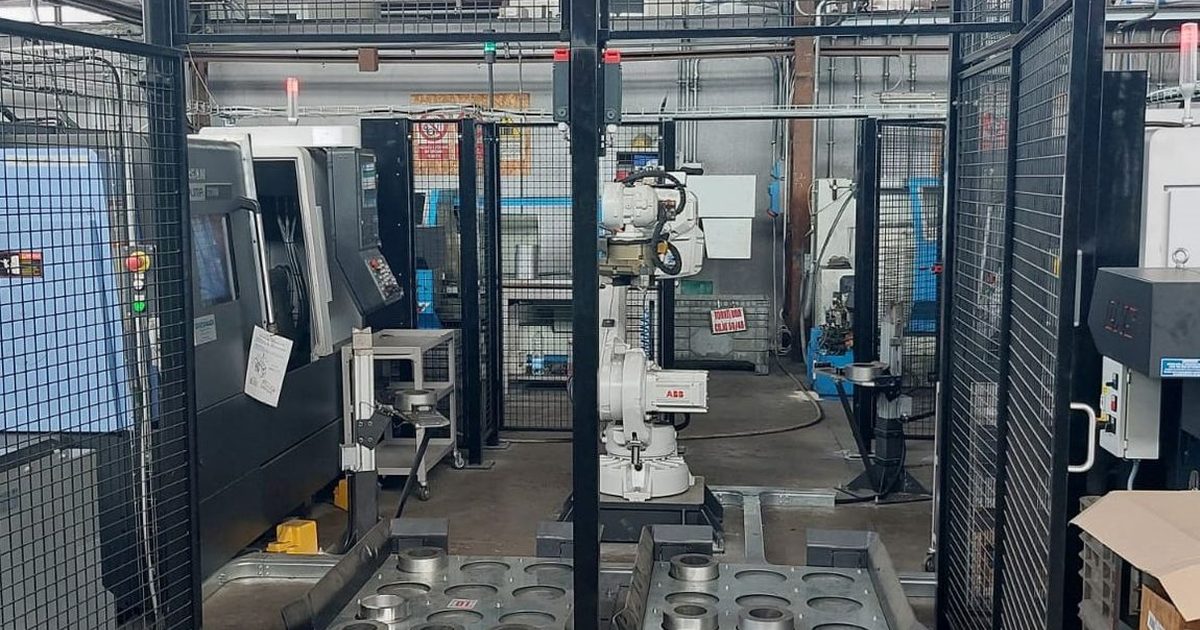 Isola di asservimento: robot ABB recintato tra due torni, con il pallet dei pezzi in primo piano